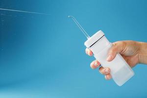 Irrigator in der Hand zum Reinigen des Mundes mit einem Schuss Wasserstrahl auf blauem Hintergrund foto