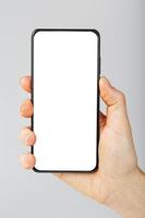 Hand hält schwarzes Smartphone mit leerem weißem Bildschirm und modernem rahmenlosem Design isoliert auf grauem Hintergrund. foto