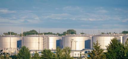 Blick auf Kraftstofftanks, Ölraffinerieanlage im morgendlichen Tageslicht gegen grüne Sommerbäume und blauer Himmel foto