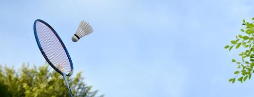 Badmintonschläger und weißer Federball mit Bluesky- und Baumhintergrund, Badmintonspiel im Freien im Freizeit- und Freizeitaktivitätskonzept, weicher und selektiver Fokus. foto