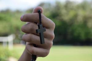 asiatischer junger christlicher junge zeigt seine hölzerne rosenkranzkette mit einem kreuz, weichem und selektivem fokus, konzept, um anderen menschen auf der ganzen welt stolz darauf zu zeigen, christ zu sein. foto