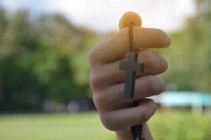 asiatischer junger christlicher junge zeigt seine hölzerne rosenkranzkette mit einem kreuz, weichem und selektivem fokus, konzept, um anderen menschen auf der ganzen welt stolz darauf zu zeigen, christ zu sein. foto