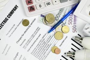 Taschenrechner und Euro-Scheine mit Stift auf europäischer Stromrechnung. konzept, geld zu sparen, indem energiespar-led-glühbirnen und die zahlung von stromrechnungen verwendet werden foto