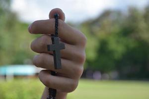 asiatischer junger christlicher junge zeigt seine hölzerne rosenkranzkette mit einem kreuz, weichem und selektivem fokus, konzept, um anderen menschen auf der ganzen welt stolz darauf zu zeigen, christ zu sein. foto