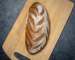 Laib Schwarzbrot auf einem Küchenbrett. Brot auf schwarzem Hintergrund. gesundes Essen. foto