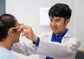 selektiver fokus auf das gesicht des optikers. während der Arzt mit Optometriegeräten und einem Testbrillengestell das Augensehsystem älterer Patientinnen mit professioneller Maschine und Technik untersucht. foto