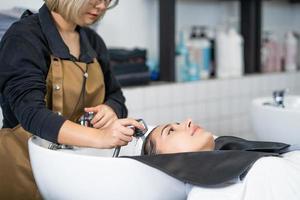 schöne kaukasische frauen fühlen sich entspannt und wohl, während sie sich mit shampoo und massage die haare waschen. friseurstudio mit stilvollem haar, schönheits- und modekonzept. foto