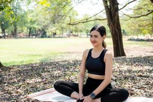 Selektiver Fokus auf das Gesicht junger schöner asiatischer Frauen, die beim Aufwärmen vor dem Yoga mit Natur und Bäumen im Hintergrund lächeln. Gesunder Lebensstil für einen guten Körper- und Gesundheitszustand. foto