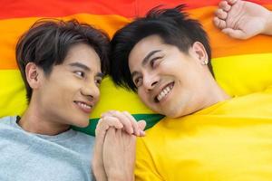 Porträt eines jungen schwulen homosexuellen Paares, das sich zusammen auf dem Bett mit bunter Flagge im Hintergrund hinlegt. Glücksmoment von Bisexuellen. Gleichstellung der Geschlechter und Menschenrechtskonzept. foto