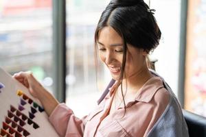 konzentrieren sie sich auf die farbkarte. junge hübsche asiatische frauen, die im friseursalon sitzen und lächeln, während sie neue haarfärbemittelfarbe und -stil aus der farbkartenauswahl auswählen. weibliche schönheitsmode, körperpflegekonzept foto