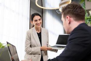 selektiver fokus auf dem computerbildschirm. kaukasische geschäftsfrauen kleiden sich in einem formellen anzug, der einen laptop-computer hält, während sie sich mit einem lächeln und selbstbewusst über ein arbeitsprojekt mit dem chef treffen. Indoor-Büroarbeit erschossen. foto