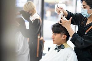 asiatische männer haare stilvoll mit dem kunden, während sie die haare schneiden und eine chirurgische gesichtsmaske tragen, während sie das haar für den kunden stylen. Berufliche Tätigkeit, Schönheits- und Modeservice neue Normalität foto