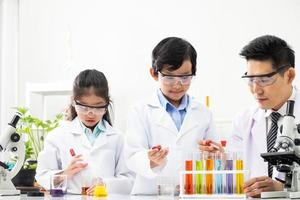 junge asiatische kinder, die weißes wissenschaftlerkleid tragen und während des studiums chemische reagenzgläser machen, lernen im naturwissenschaftlichen klassenzimmer mit dem lehrer. Kleinkinderbildungskonzept durch Experiment, Spaß und Spaß im Klassenzimmer foto