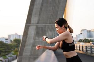 selektiver fokus auf das gesicht junger schöner asiatischer frauen, die eine intelligente uhr verwenden, um aktivitäten zu verfolgen und musik zu hören, während sie sich vor dem training aufwärmen oder mit blick auf die stadt rennen. fitter und gesunder Lebensstil. foto