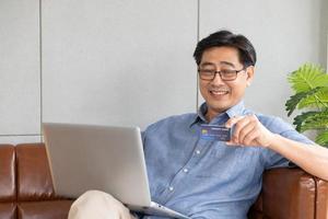 selektiver Fokus auf Kreditkarte. ältere asiatische männer halten kreditkarte in der hand und füllen zahlungsinformationen für online-einkäufe aus. drahtlose internettechnologie mit älterem konzept. foto