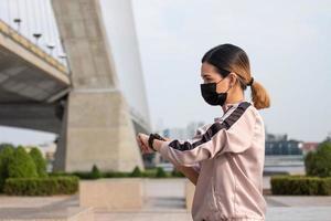 Selektiver Fokus auf das Gesicht junger schöner asiatischer Frauen, die eine chirurgische Gesichtsmaske tragen, während sie sich vor dem Training aufwärmen oder morgens im Park laufen. neuer normaler lebensstil. foto