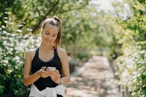 aktive sportliche erwachsene frau in sportbekleidung track fitnessaktivität über smartphone überwacht die gesundheit mit der besten fitnessanwendung hat dunkle gekämmte haarposen im freien. sport gesundes lebensstilkonzept foto