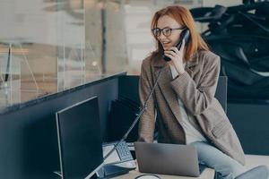 Frau mit Brille telefoniert, während sie an ihrem Arbeitsplatz im Büro sitzt foto