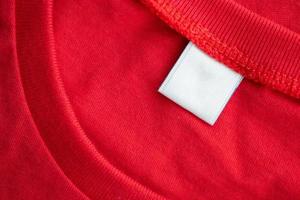 weißes leeres Kleidungsetikett auf neuem rotem Baumwollhemd-Stoff-Texturhintergrund foto
