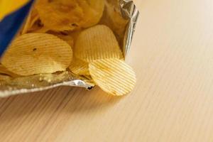 Knusprige Kartoffelchips in Snackbeutel auf Holztisch foto