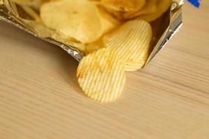 Knusprige Kartoffelchips in Snackbeutel auf Holztisch foto