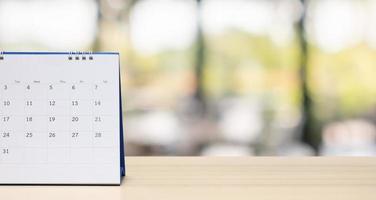 Tischkalender aus weißem Papier auf Holztisch mit verschwommenem Bokeh-Hintergrund, Termin- und Geschäftstreffenkonzept foto