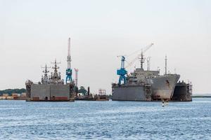 Große eiserne Marineschiffe in der Werft zur Reparatur. Großer Kran in der Werft. Hafen am blauen Meer foto