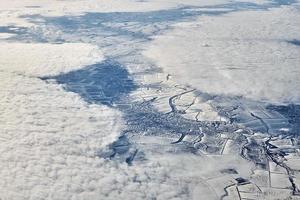 luftaufnahme über wolkenoberseite zu schneebedeckten flüssen, feldern und straßen, winterfrische frostige luft foto