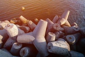 Tetrapoden-Wellenbrecher im Meerwasser. Wunderschöne Sonnenuntergangslandschaft mit Tetrapoden aus Beton zum Schutz von Küstenstrukturen vor Sturmwellen, Wettereinflüssen und Küstendrift foto