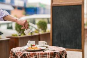 Der Koch gießt Sirup auf Pfannkuchen mit Beeren auf dem Serviertisch zum Frühstück foto