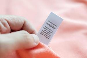 hand halten und lesen bei weißer wäschepflege waschanleitung kleidungsetikett auf rosa hemd foto