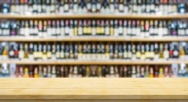 leere holztischplatte mit unscharfen weinflaschen auf alkoholregalen im supermarkt-weinladenhintergrund foto