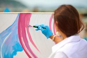 Künstlerin, die an abstraktem Ölgemälde im Freien arbeitet, Hand mit Pinsel, große Leinwand foto