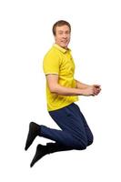 lustiger attraktiver Kerl im gelben T-Shirt und in den blauen Hosen, die lokalisiert auf weißem Hintergrund springen foto