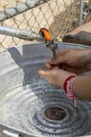 Eine Frau wäscht sich draußen in einem provisorischen Waschbecken aus Metall und Rohren die Hände. Mexiko foto