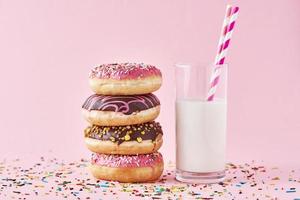 Stapel bunter Donuts dekoriert und Glas Milch auf rosa Hintergrund foto