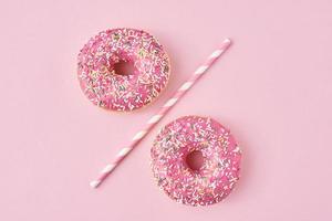 zwei donuts getrennt mit einem trinkhalm auf rosa hintergrund. kreatives Essenskonzept foto