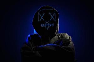 anonymer mann im kapuzenpulli, der das gesicht hinter der gruseligen maske des neonlichts versteckt. Horror-Konzept foto
