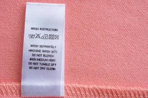 Weiße Wäschepflege Waschanleitung Kleideretikett auf rosa Baumwollhemd foto