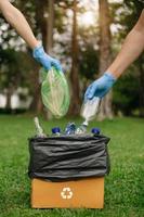 leute halten müllflasche plastik und glas in der hand und legen sie in den recyclingbeutel. reinigung, verschmutzung, ökologie und konzept. foto