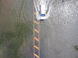 Überschwemmte Straßen, Menschen mit Autos, die durchfahren. Drohnenaufnahmen aus der Luft zeigen überschwemmte Straßen und vorbeifahrende Autos, die Wasser spritzen. foto