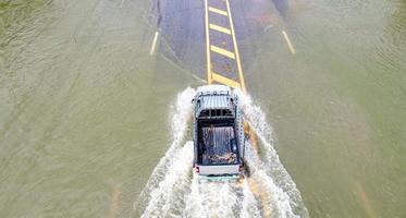 Überschwemmte Straßen, Menschen mit Autos, die durchfahren. Drohnenaufnahmen aus der Luft zeigen überschwemmte Straßen und vorbeifahrende Autos, die Wasser spritzen. foto