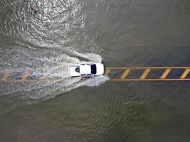 Überschwemmte Straßen, Menschen mit Autos, die durchfahren. Drohnenaufnahmen aus der Luft zeigen überschwemmte Straßen und vorbeifahrende Autos, die Wasser spritzen. foto