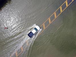Überschwemmte Straßen, Menschen mit Autos, die durchfahren. Drohnenaufnahmen aus der Luft zeigen überschwemmte Straßen und vorbeifahrende Autos, die Wasser spritzen. foto