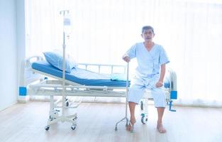 der kranke oder ältere asiatische alte mann konnte nicht alleine auf dem bett des patienten sitzen und mit einem gehstock auf den arzt und die krankenschwester zur behandlung oder heilung im krankenhaus oder im gesundheitswesen warten foto