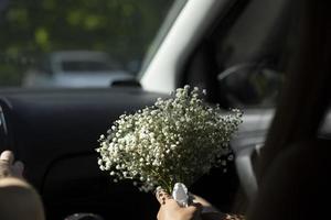Blumenstrauß im Auto. Brautstrauß ist in den Händen des Mädchens. weiße Blumen in der Hand. foto
