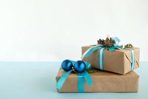Zwei Weihnachtsgeschenkboxen aus Kraftpapier, blaue und weiße Bänder, verziert mit Tannenzweigen, Tannenzapfen und Weihnachtskugeln auf blauem und weißem Hintergrund. Platz kopieren. foto