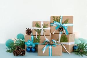 weihnachtsgeschenkboxen aus bastelpapier, blaue und weiße bänder auf dem blau-weißen hintergrund, verziert mit tannenzapfen, tannenzweigen, weihnachtskugel und lichtern. foto