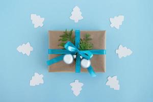 Geschenkbox aus Bastelpapier, blauem Band und verzierten Tannenzweigen und silbernen Weihnachtskugeln mit weißem Papiertannenbaum auf blauem Hintergrund, Draufsicht. Weihnachtsgeschenk. foto