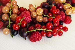 gemischte sommerbeeren - himbeere, schwarze johannisbeere, rote johannisbeere, weiße johannisbeere, stachelbeere, kirsche - auf dem weißen hölzernen hintergrund. foto